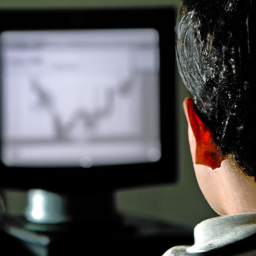 description: an anonymous image of a young adult sitting at a computer, with a chart of stock prices on the screen in front of them.