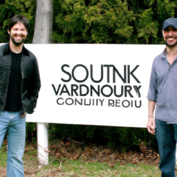 description: a photo of ashton kutcher and guy oseary standing in front of a sound ventures sign. they are both wearing casual clothes and smiling. the image is taken outdoors, and there are trees in the background.