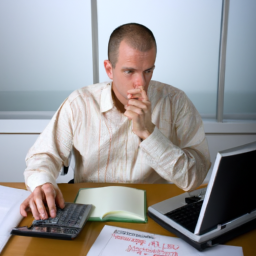 a person sitting at their desk with a laptop and a notebook, surrounded by financial documents and a calculator. they appear to be deep in thought as they consider their investment options.
